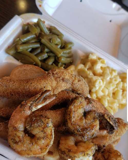 A takeout container with fried shrimp, macaroni and cheese, green beans, and a slice of bread.