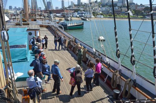A group of people on the deck of a ship, with a view of the waterfront and city skyline in the background.