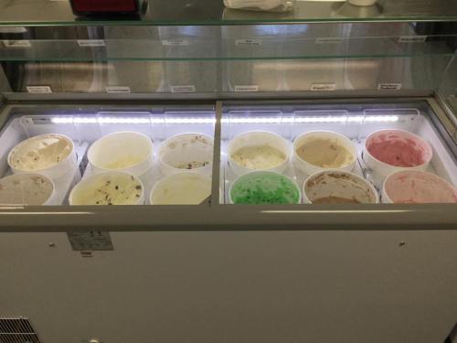 A display of various ice cream tubs in a freezer, showcasing different flavors in a well-lit setting.