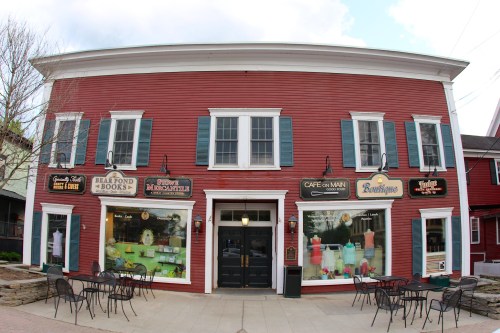 A red building with white trim features shops and outdoor seating, set against a cloudy sky.