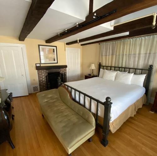 Cozy bedroom with a wooden beam ceiling, a large bed, a green bench, and a fireplace. Warm, inviting atmosphere.
