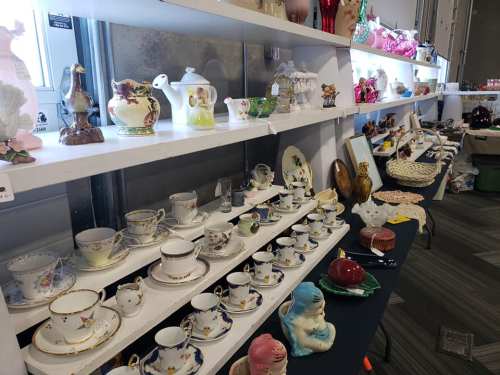 A display of vintage ceramics and collectibles on shelves, including teapots, figurines, and decorative plates.