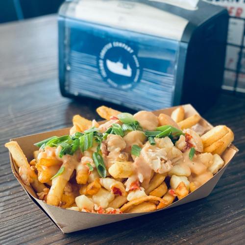 A serving of loaded fries topped with cheese, gravy, and green onions in a paper tray on a wooden table.