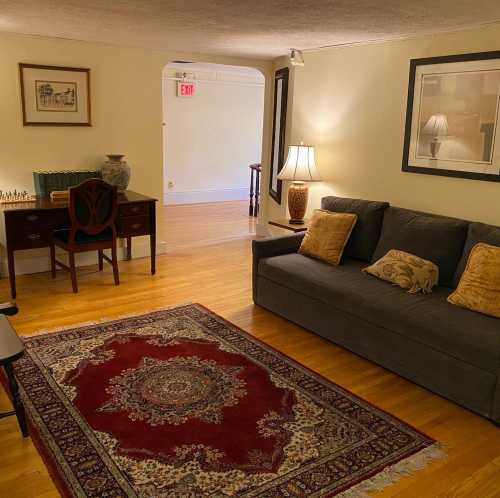 Cozy living room with a sofa, lamp, chess set, and a decorative rug, featuring warm lighting and wooden floors.