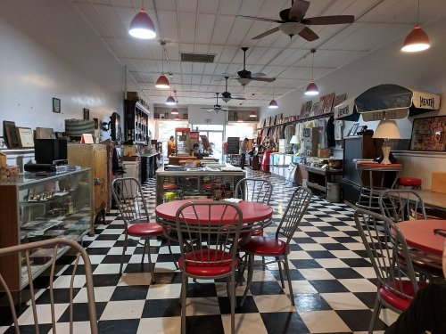 A vintage diner interior with checkered floors, red and silver tables, and retro decor lining the walls.