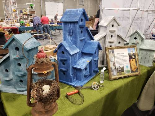 Colorful birdhouses in various sizes displayed on a table, alongside vintage items and a framed informational sign.