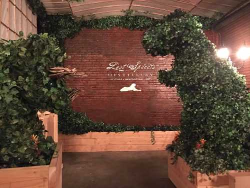 A brick wall adorned with greenery features a large, leafy dinosaur sculpture at Lost Species Distillery.