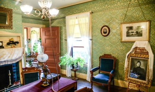 A vintage room with green wallpaper, antique furniture, a chandelier, and framed photos, creating a nostalgic atmosphere.