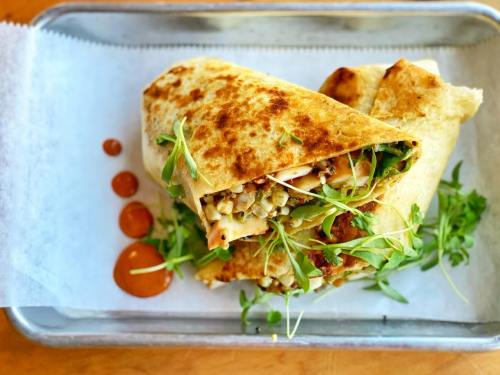 A grilled wrap filled with greens and chicken, served on a tray with sauce and garnished with microgreens.