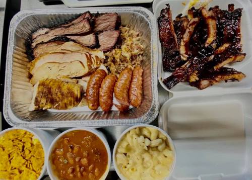 A variety of barbecue meats including brisket, chicken, ribs, and sausages, served with sides of beans and macaroni.