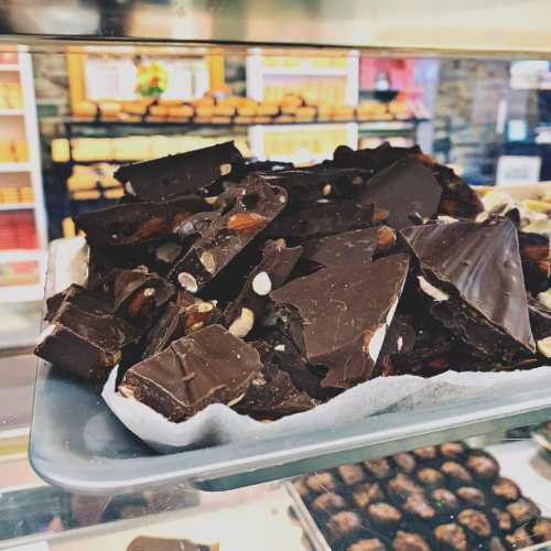 A close-up of a tray filled with dark chocolate pieces mixed with nuts, displayed in a shop.