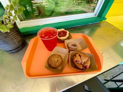 A tray with a drink and four baked goods, including cookies and fruit pastries, on a metal table.