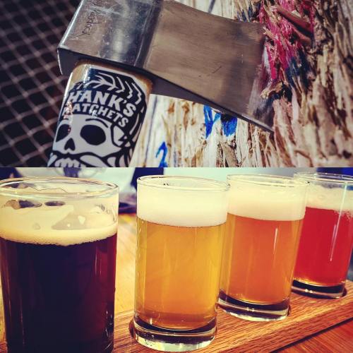 A close-up of an axe embedded in wood, with four glasses of different beers in the foreground.