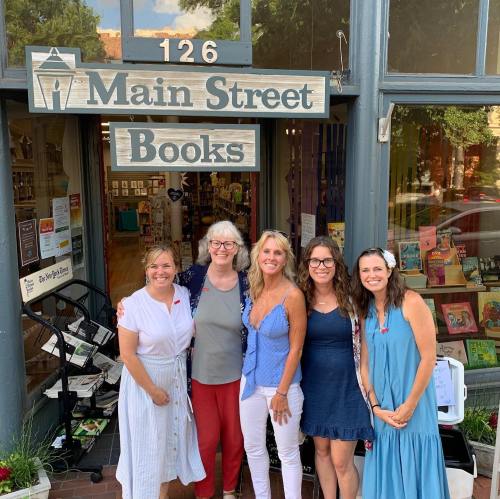 Five women stand in front of Main Street Books, smiling and posing together outside the store.