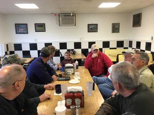 A group of men sitting around a table in a diner, engaged in conversation, with condiments on the table.