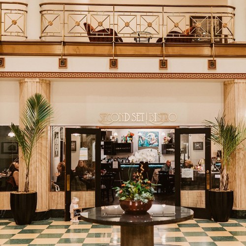 Elegant restaurant interior with potted plants, a bar area, and diners enjoying their meals in a stylish setting.