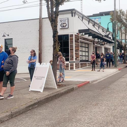 A line of people waiting outside a building on a sidewalk, with a sign indicating a waitlist nearby.