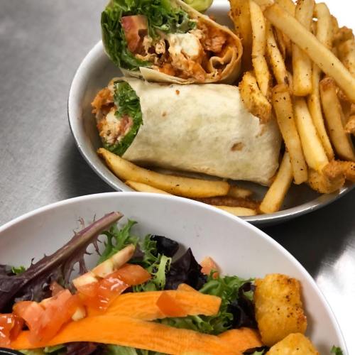 A plate with a wrap filled with lettuce and chicken, alongside a bowl of salad and a serving of golden fries.