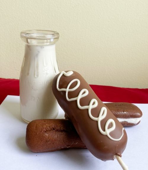 A glass bottle of milk next to two chocolate-covered snack cakes with white icing on top.