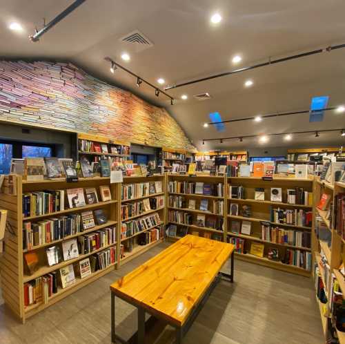 A cozy bookstore interior with wooden shelves filled with books and a central wooden table under warm lighting.