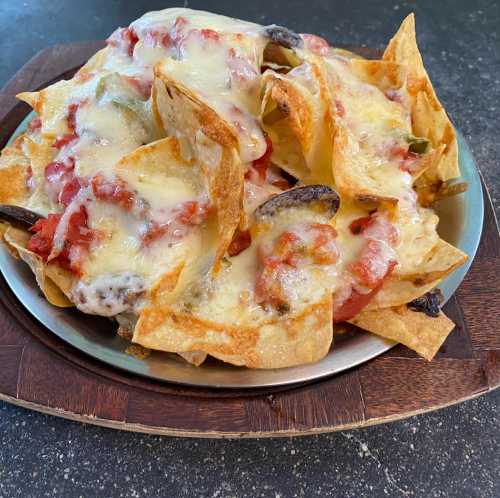 A plate of cheesy nachos topped with melted cheese, tomatoes, and black olives on a wooden serving board.