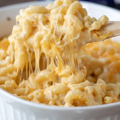 A close-up of creamy, cheesy macaroni and cheese being lifted with a wooden spoon, showcasing its gooey texture.