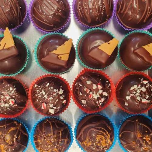 A colorful assortment of chocolate truffles, topped with various decorations like peppermint and caramel pieces.