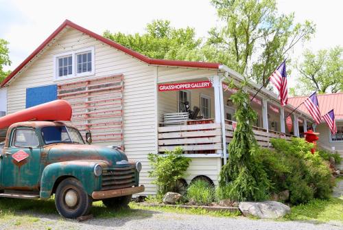 A vintage truck parked outside a gallery with red accents and American flags, surrounded by greenery.