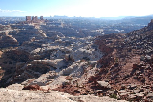 A vast desert landscape with layered rock formations and distant mesas under a clear blue sky.