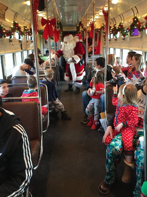 A festive train interior filled with children in pajamas, with Santa Claus interacting with them amidst holiday decorations.