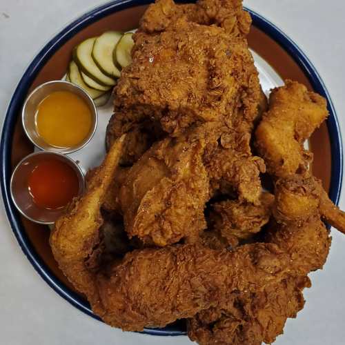 A plate of crispy fried chicken with pickles and two dipping sauces on the side.