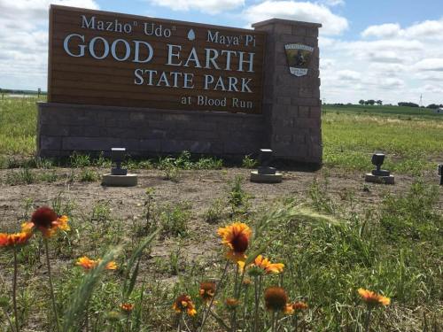 Sign for Good Earth State Park at Blood Run, surrounded by green grass and wildflowers under a blue sky.