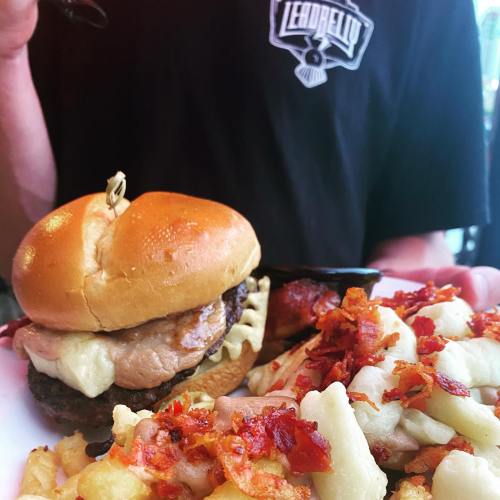 A close-up of a burger with a patty and toppings, served with a side of bacon-topped gnocchi.