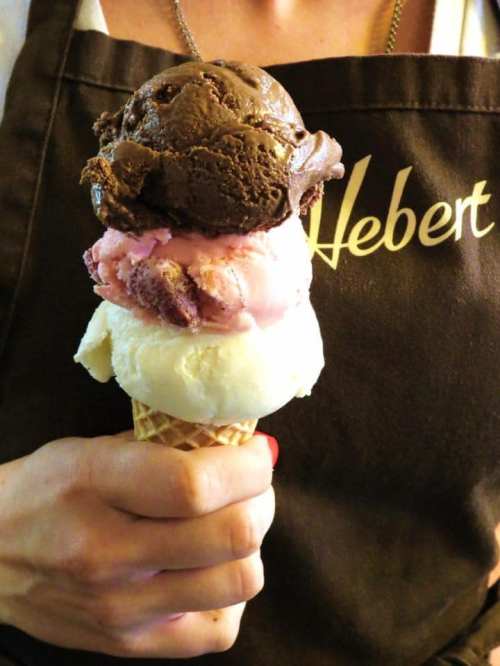 A hand holding a triple scoop ice cream cone with chocolate, raspberry, and vanilla flavors.