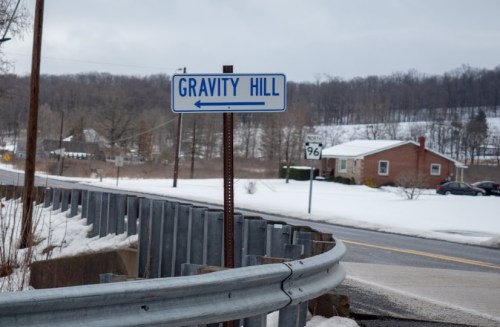 A sign for "Gravity Hill" points left, with a snowy landscape and a house in the background.