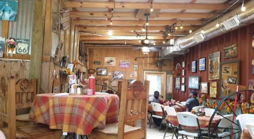 Cozy restaurant interior with wooden decor, checkered tablecloths, and vintage wall art. Patrons seated at tables.