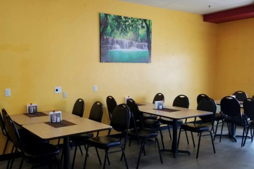A bright yellow dining area with black chairs and tables, featuring a nature-themed painting on the wall.