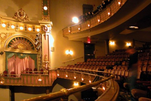Interior of a vintage theater with ornate decor, empty seats, and a stage partially visible in the background.
