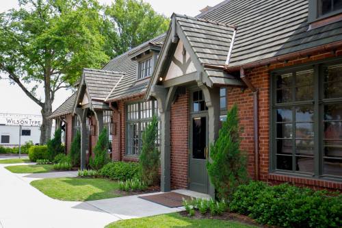 Charming brick buildings with sloped roofs and green landscaping along a sidewalk on a sunny day.