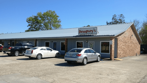 A brick building with a blue exterior and a sign reading "Dempsey's," featuring parked cars in front.