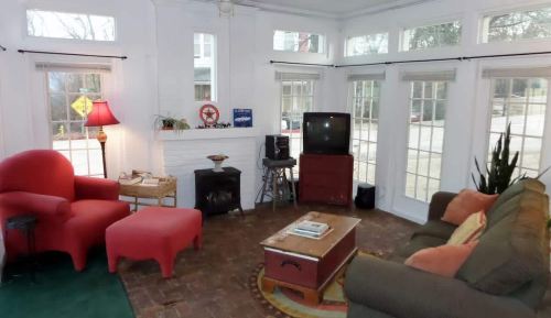 Cozy sunroom with large windows, red chairs, a green sofa, a coffee table, and a TV on a wooden stand.