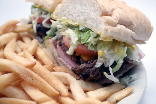 A close-up of a sandwich filled with lettuce, tomato, and meat, served with a side of golden French fries.