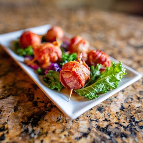 A plate of bacon-wrapped meatballs on a bed of greens, garnished with purple cabbage, on a granite countertop.