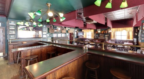 A cozy bar interior with green lamps, wooden counters, and framed photos on the walls, creating a warm atmosphere.