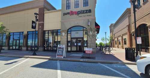 Exterior of Pure Fire Pizza restaurant with outdoor seating and a sign in front, located in a shopping area.