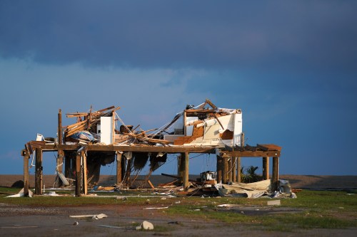 A heavily damaged house with a collapsed roof and exposed interior, set against a cloudy sky.