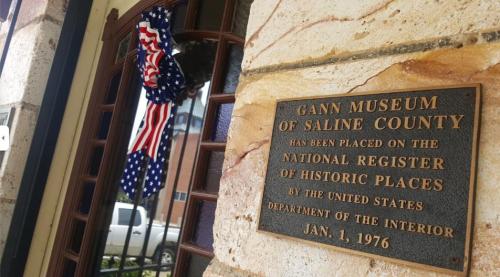 Plaque on a stone wall indicating the Gann Museum of Saline County is a historic site, with a patriotic wreath nearby.