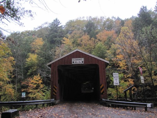 A red covered bridge surrounded by autumn foliage, with clearance and weight limit signs visible.