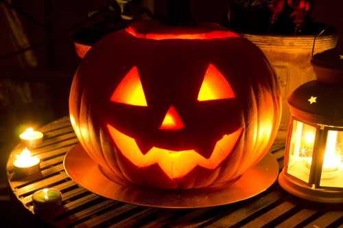 A carved pumpkin with a smiling face, glowing from within, surrounded by candles and a lantern on a table.