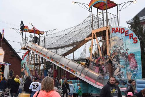 A colorful carnival slide with a pirate theme, surrounded by people enjoying the fair on a cloudy day.